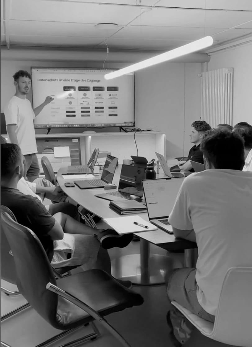 Ein bauklar-Kurs vor Ort: Am Bildschirm läuft die Folie «Datenschutz ist eine Frage des Zugangs», das Team sitzt mit Laptops um den Tisch.